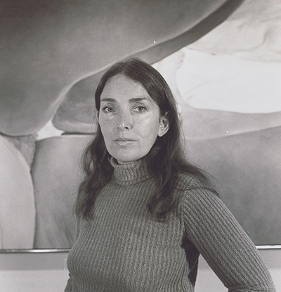 Grayscale portrait of a woman with medium-length hair wearing a turtleneck sweater and standing in front of a large painting depicting a woman reclining.